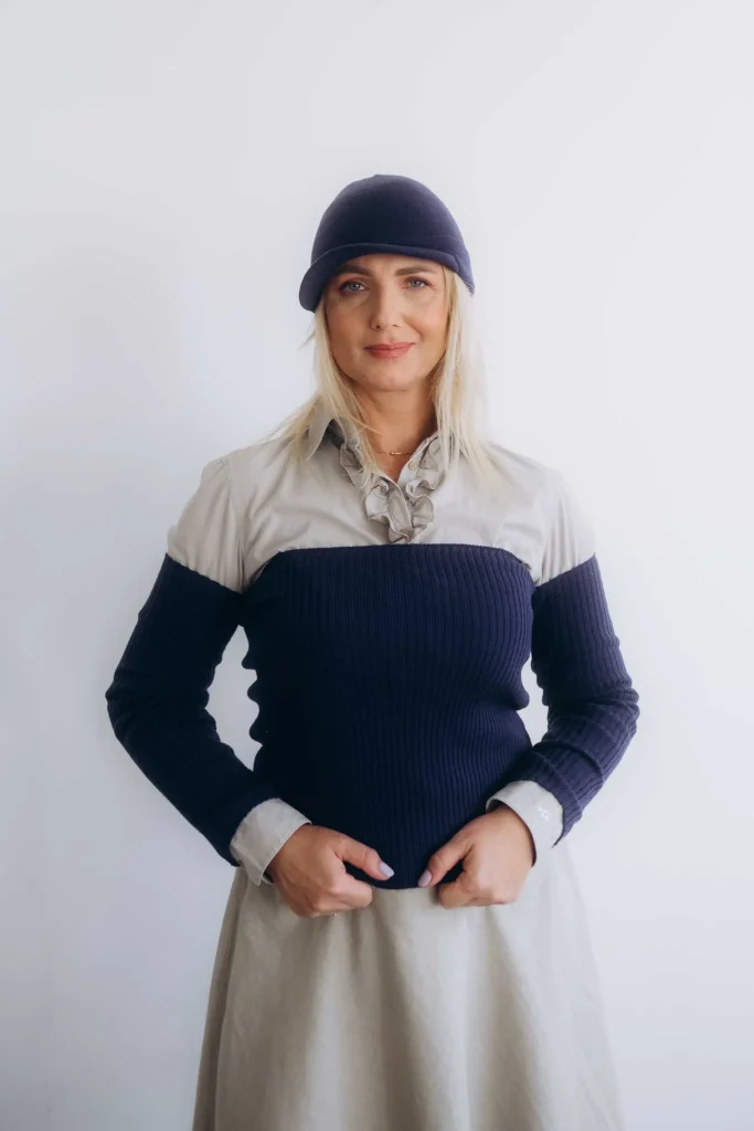 Žena v tmavomodrom trojsete TATTJA – nákrčník, rukávniky a čiapka so šiltom z merino vlny, elegantný predný pohľad.