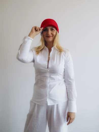 Modelka v bielom outfite TATTJA s červenou pletenou čiapkou ANJA, pohľad spredu