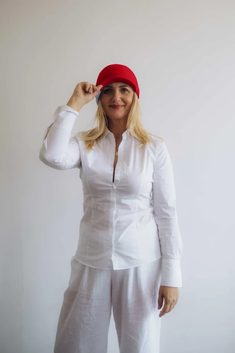 Modelka v bielom outfite TATTJA s červenou pletenou čiapkou ANJA, pohľad spredu