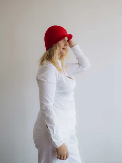 Modelka v bielom outfite TATTJA s červenou pletenou čiapkou ANJA, pohľad zboku