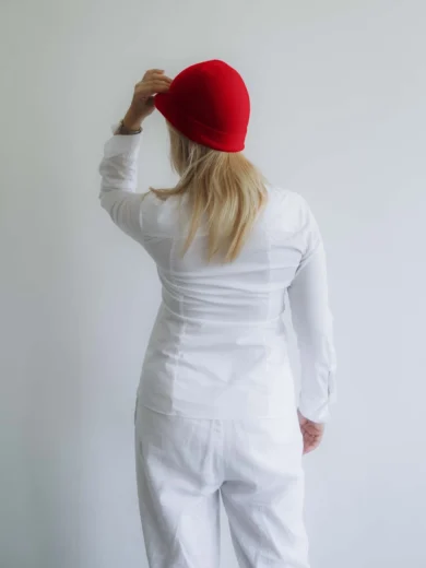 Modelka v bielom outfite TATTJA s červenou pletenou čiapkou ANJA, pohľad zozadu