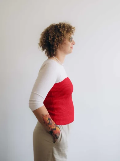 Modelka v bielom outfite TATTJA s červeným pleteným driekovníkom NATASJA, pohľad zboku