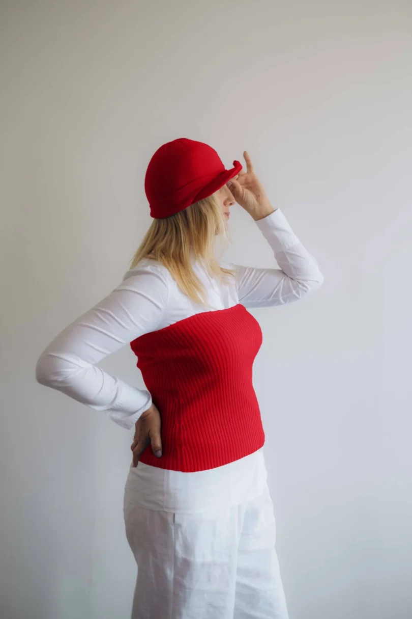 Modelka v bielom outfite s červeným pleteným dvojsetom MAGNHILD – driekovník a čiapka TATTJA, pohľad zboku