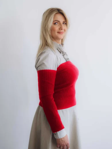 Modelka v béžovom outfite TATTJA s červeným pleteným dvojsetom SIGHRITH – driekovník a rukávniky, pohľad zboku