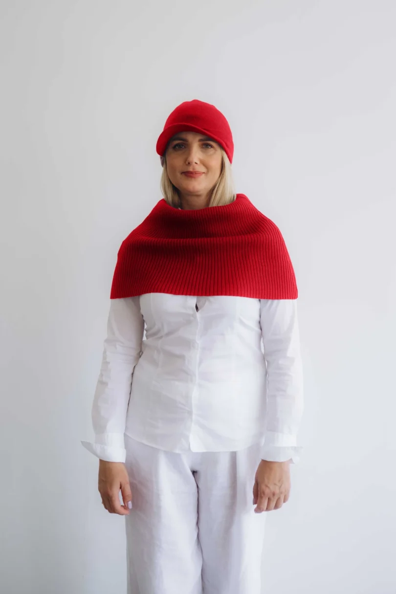 Modelka v bielom outfite TATTJA s červeným pleteným dvojsetom INGEBORG – nákrčník a čiapka, pohľad spredu