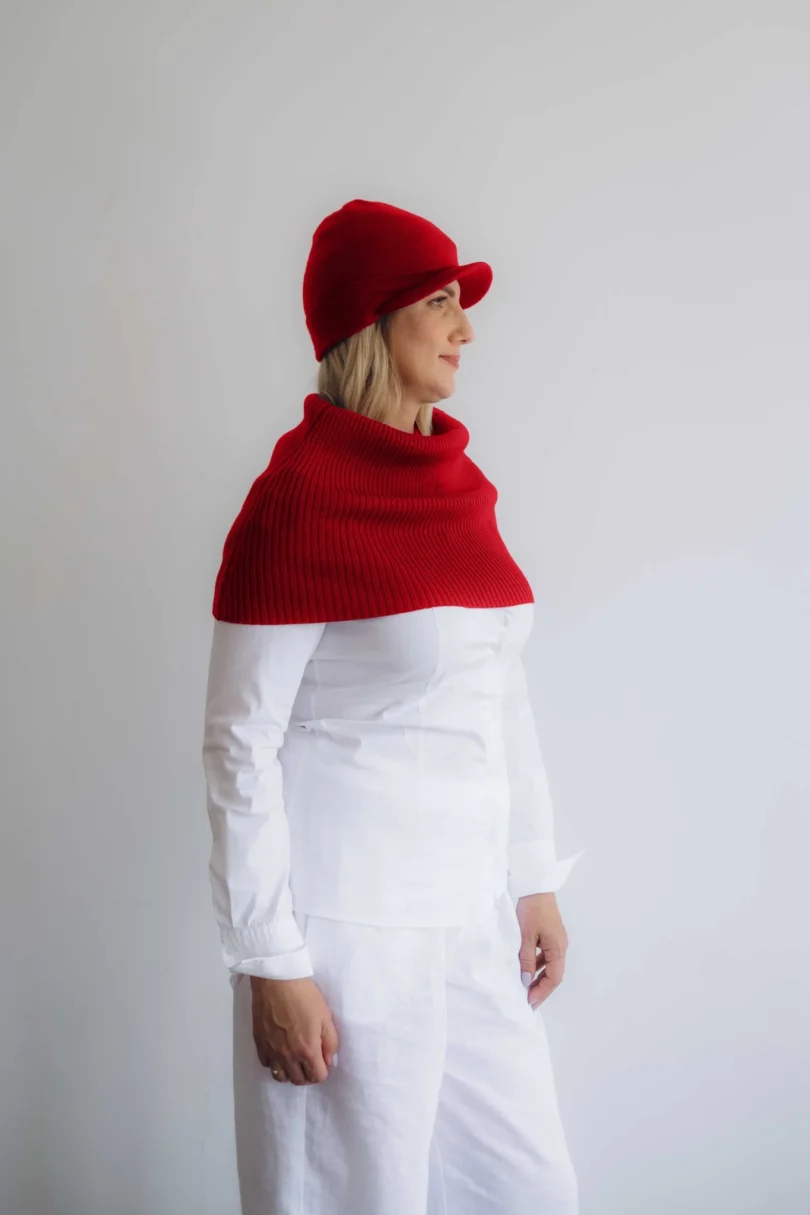 Modelka v bielom outfite TATTJA s červeným pleteným dvojsetom INGEBORG – nákrčník a čiapka, pohľad zboku