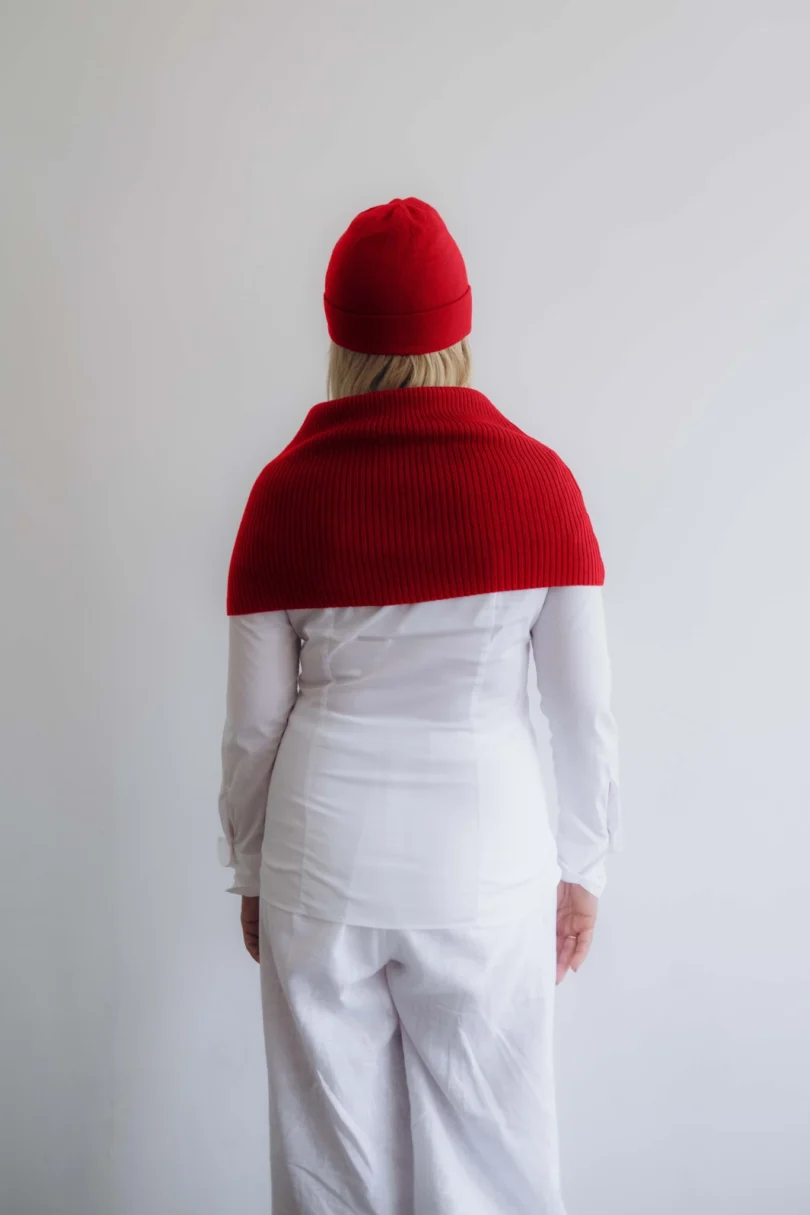 Modelka v bielom outfite TATTJA s červeným pleteným dvojsetom INGEBORG – nákrčník a čiapka, pohľad zozadu