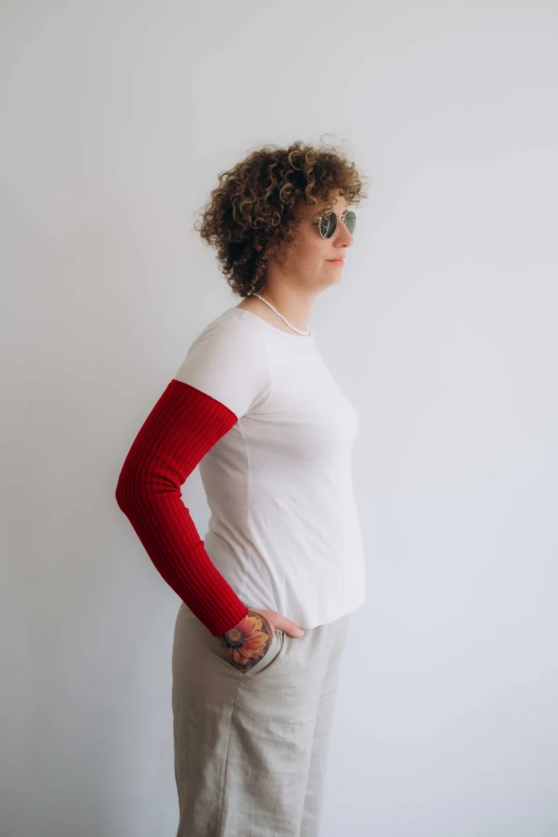 Modelka v bielom outfite s červenými pletenými rukávnikmi KATJA značky TATTJA, pohľad zboku