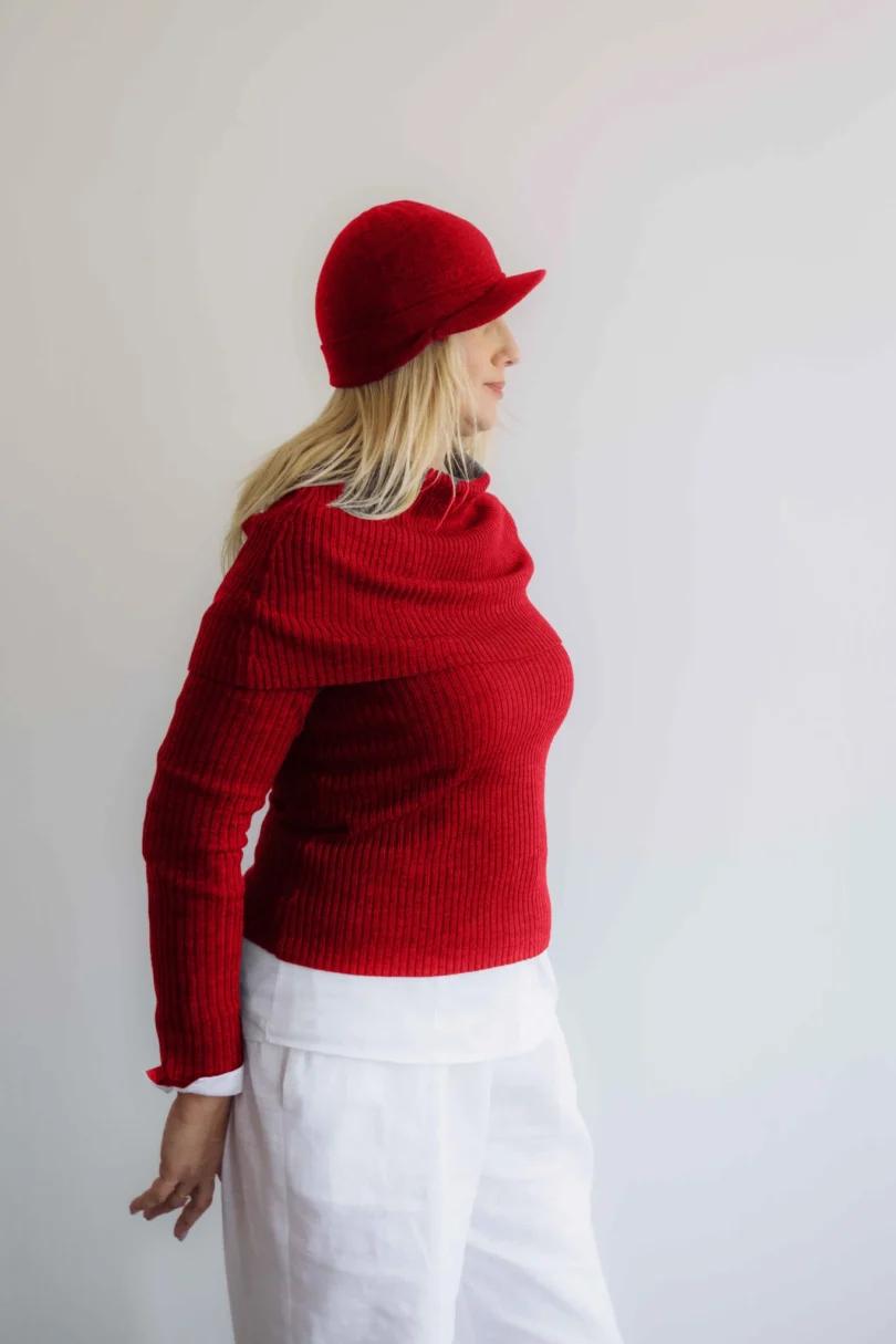 Modelka v bielom outfite s červeným pleteným štvorsetom TATTJA – nákrčník, driekovník, rukávniky a čiapka, pohľad zboku