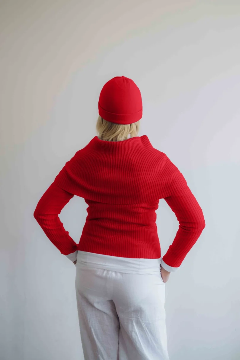 Modelka v bielom outfite s červeným pleteným štvorsetom TATTJA – nákrčník, driekovník, rukávniky a čiapka, pohľad zozadu